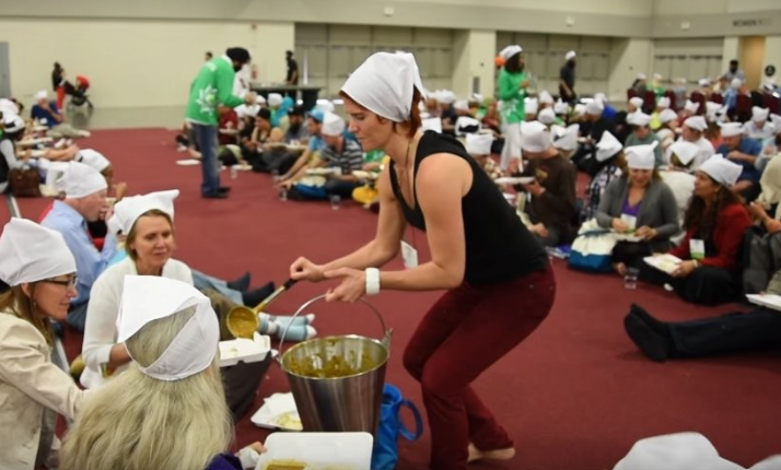 A volunteer serves food to people seated together on the floor during Langar
