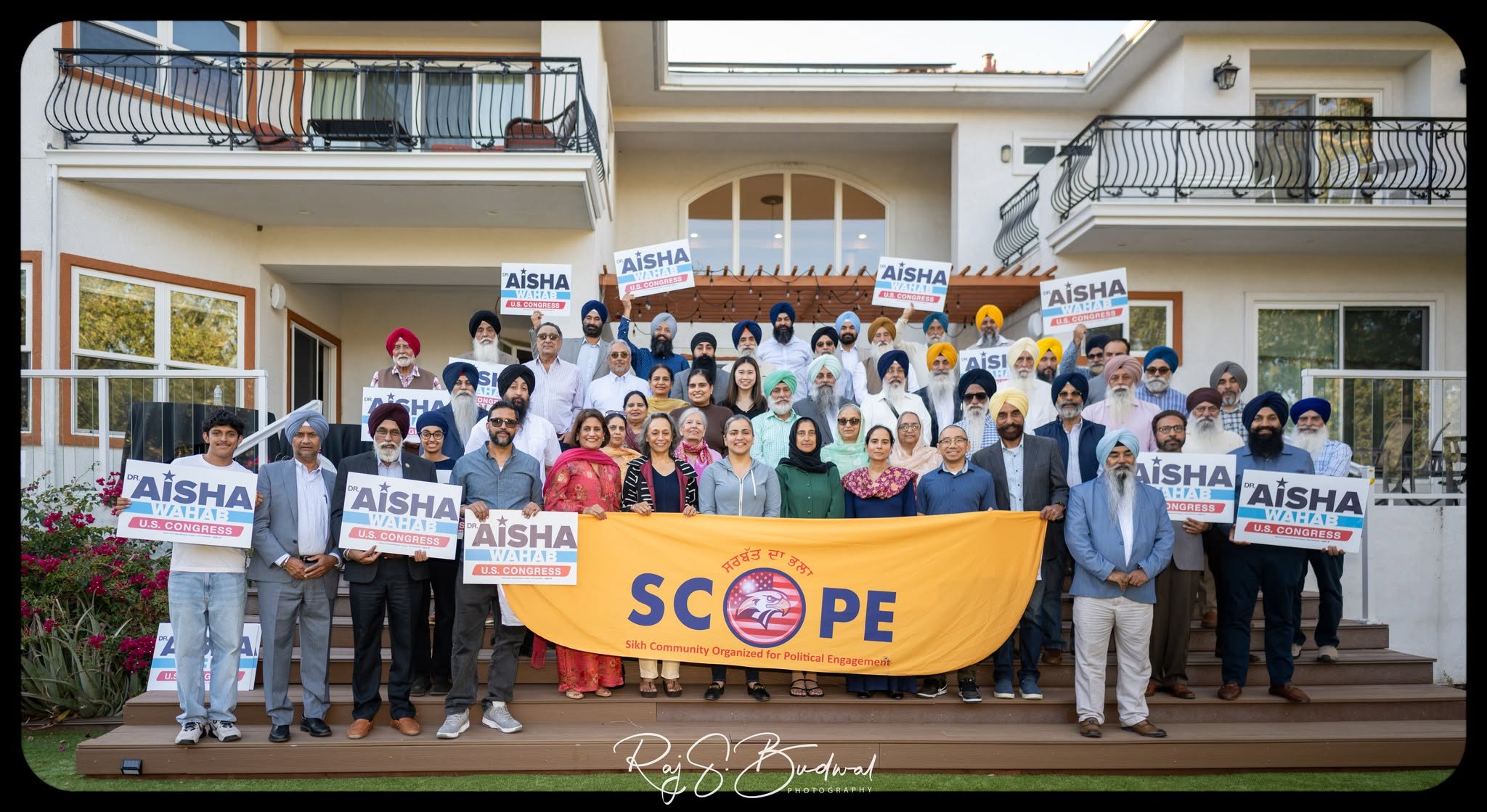 SCOPE community members gathered behind a saffron Sikh Community Organized for Political Engagement banner