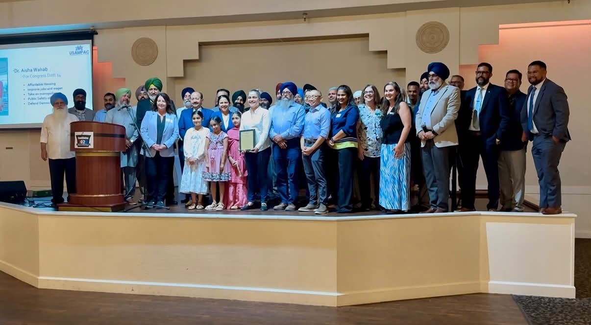 Adults and children pose on a stage beside a podium and presentation screen