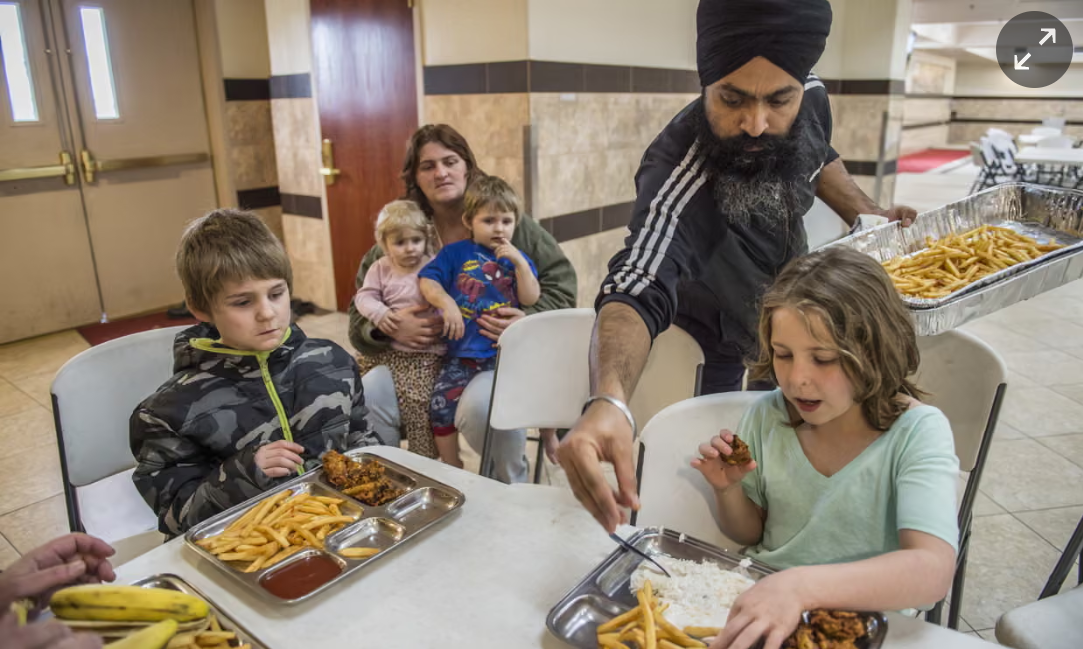 A Sikh volunteer serves a meal to children at a communal table